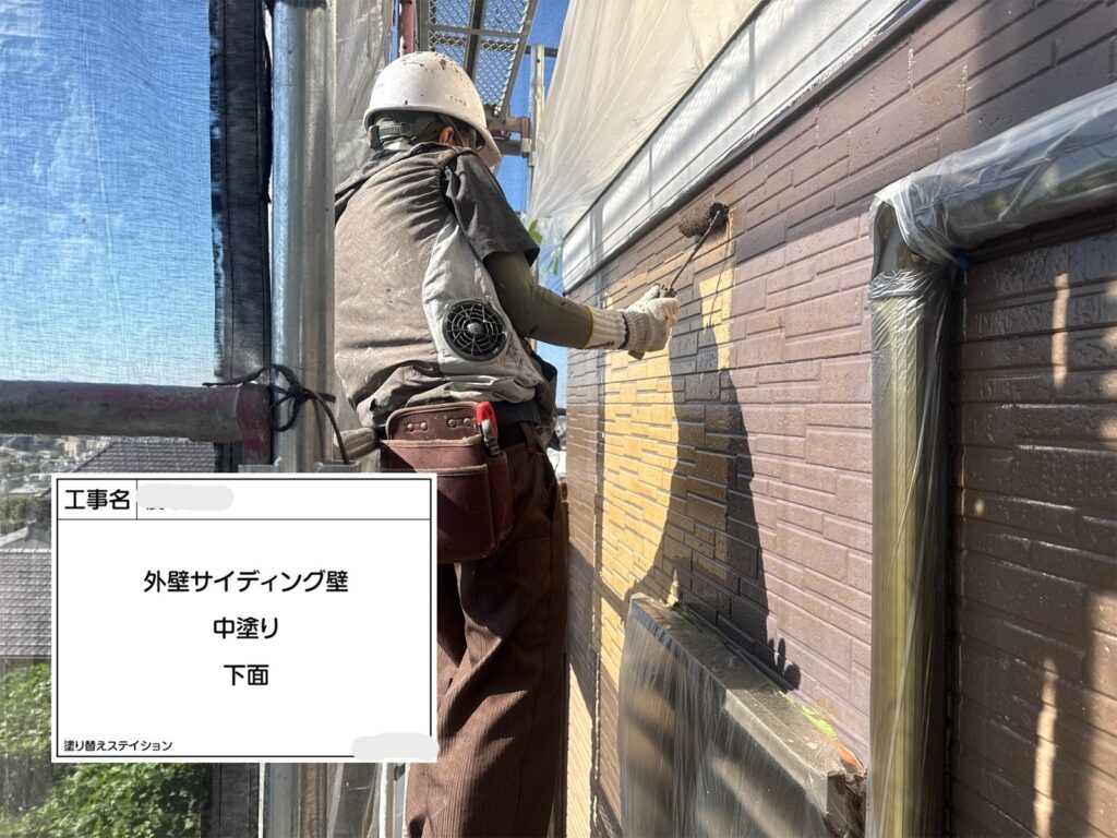 職人がローラーでサイディング外壁の中塗り塗装を行っている施工風景