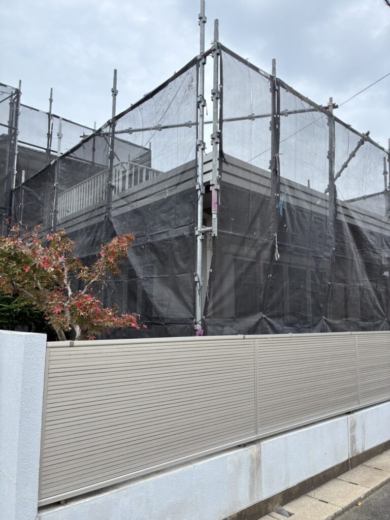 外壁塗装と屋根塗装の工事に向けて住宅の周囲に組み立てた足場と黒いメッシュシート